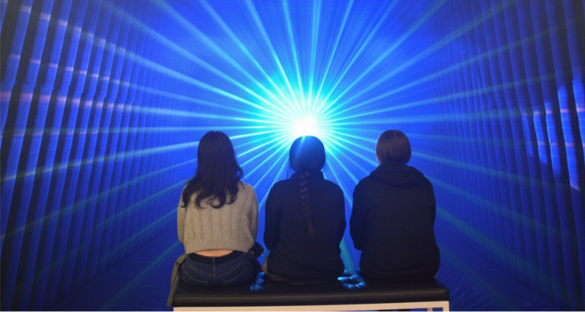 Experiencia inmersiva Jardín de Silencio de OPTIKO. Personas observando un punto de luz radiante en una estructura de arquitectura fenomenológica azul.